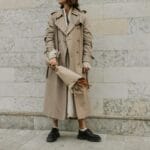 Kobieta w beżowym trenczu z bukietem kwiatów na tle marmurowej ściany