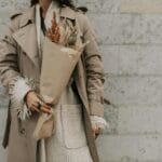 Kobieta w modnym beżowym trenczu z bukietem suchych jesiennych kwiatów