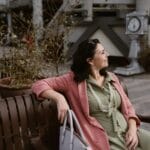 Kobieta w różowym blezerze i zielonej sukience siedzi na ławce na dworze