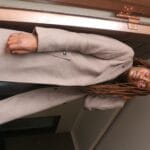 Kobieta w trenczu i okularach przeciwsłonecznych stoi przy drzwiach