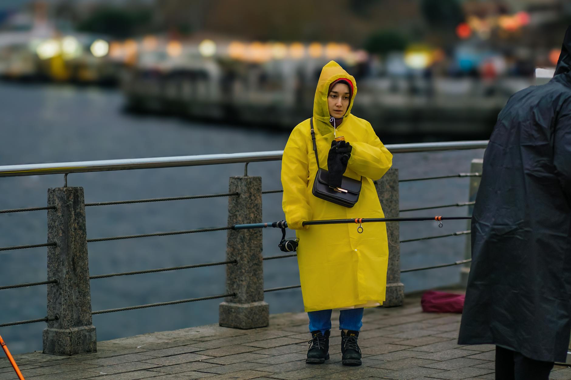 Kobieta w żółtej kurtce przeciwdeszczowej nad wodą w pochmurny dzień