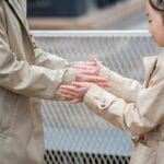 Młoda kobieta w beżowym trenczu bawi się z towarzyszem na zewnątrz