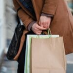 Kobieta z papierowymi torbami zakupowymi idzie ulicą miasta