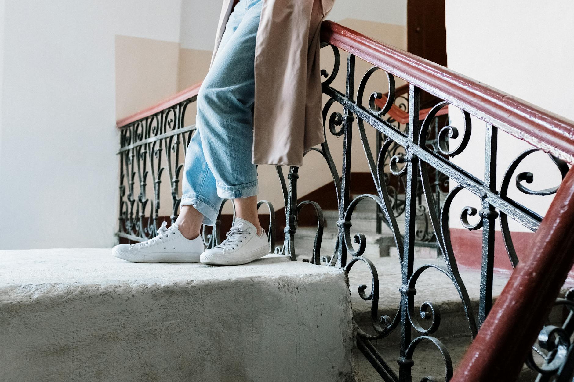 Kobieta w dżinsach w klasycznym płaszczu i sneakersach przy zabytkowej balustrad