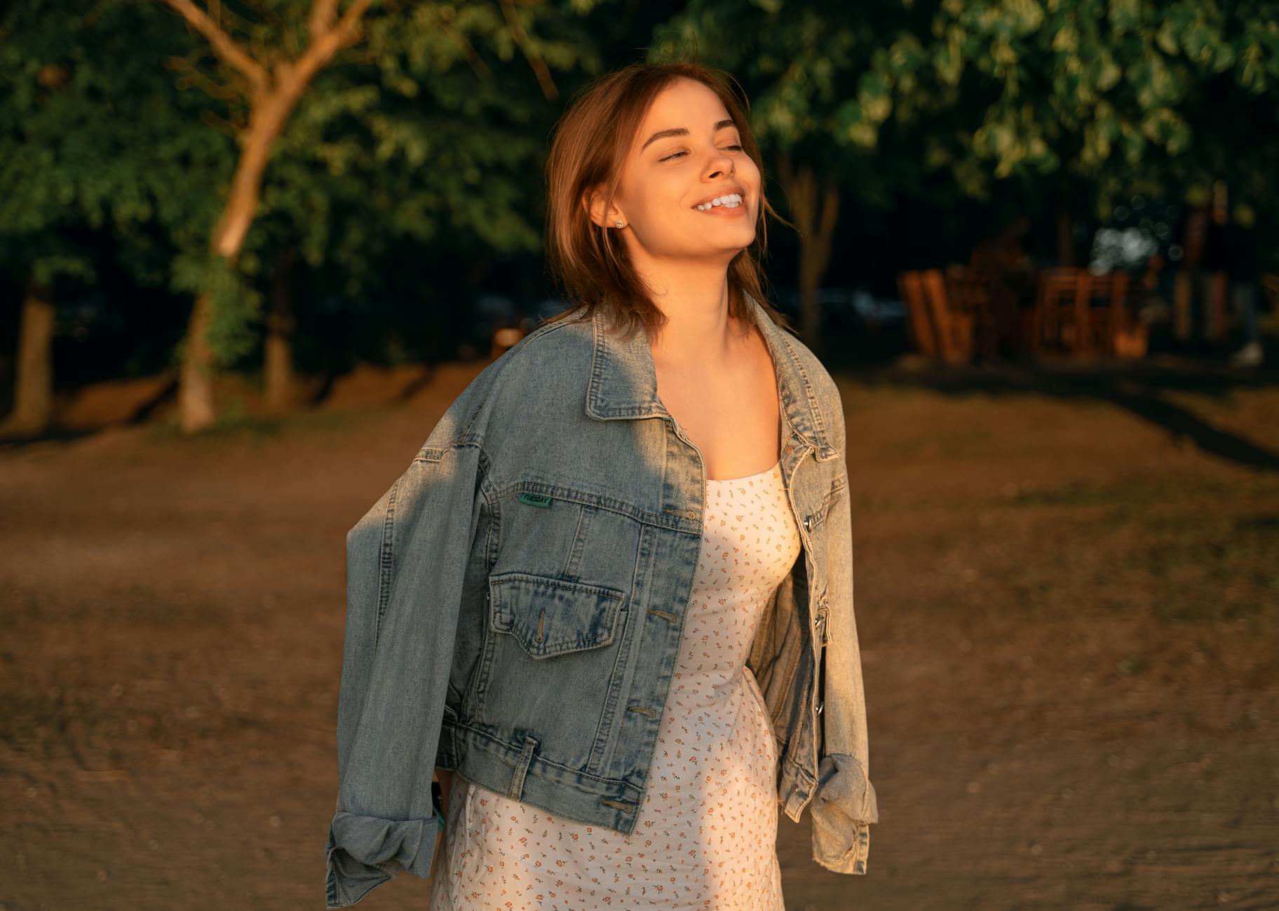 Kobieta w dżinsowej kurtce i sukience pozuje o zachodzie słońca