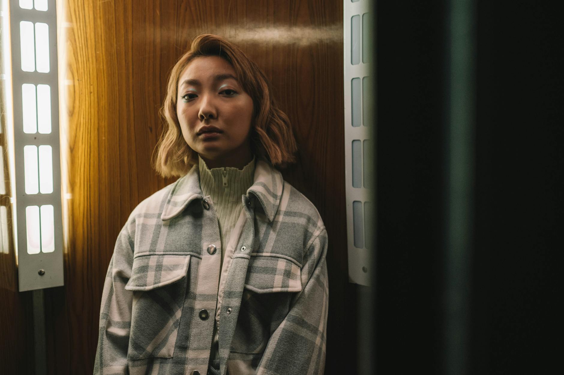 Kobieta w kraciastej koszulokurtce stoi w pomieszczeniu przy drewnianej ścianie