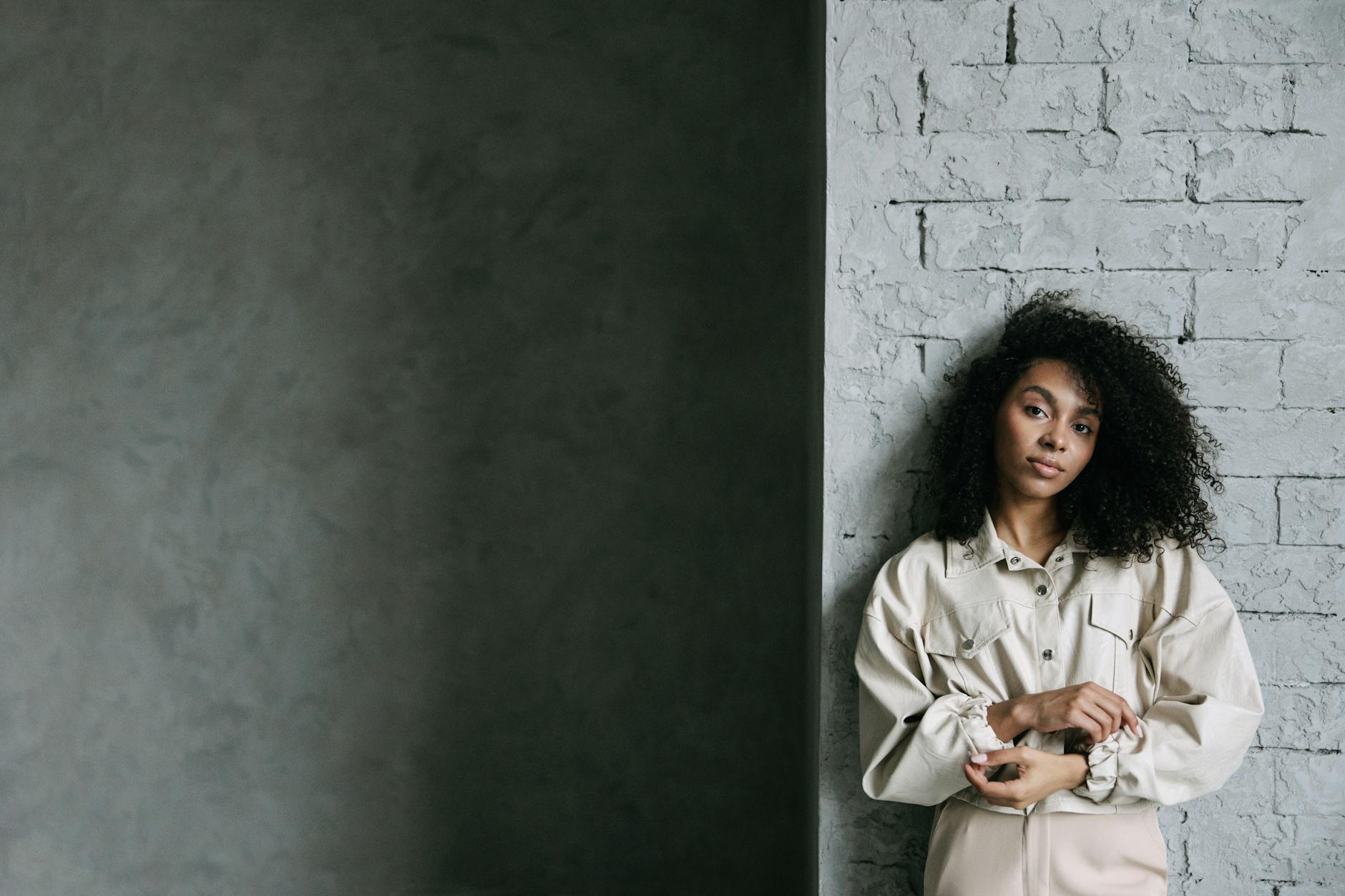 Kobieta z kręconymi włosami oparta o betonową ścianę w casualowej stylizacji