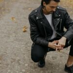 Mężczyzna w skórzanej kurtce i sneakersach na jesiennej alejce