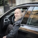 Starszy mężczyzna w zimowym płaszczu wysiadający z zaparkowanego auta