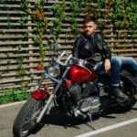 Mężczyzna w skórzanej kurtce siedzi na motocyklu przy drewnianym płocie