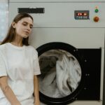 Kobieta w pralni stoi przy pralce i zastanawia się nad praniem kurtki puchowej